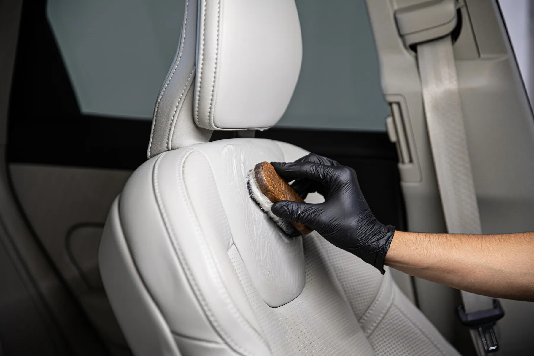 Detailer brushing a light leather car seat